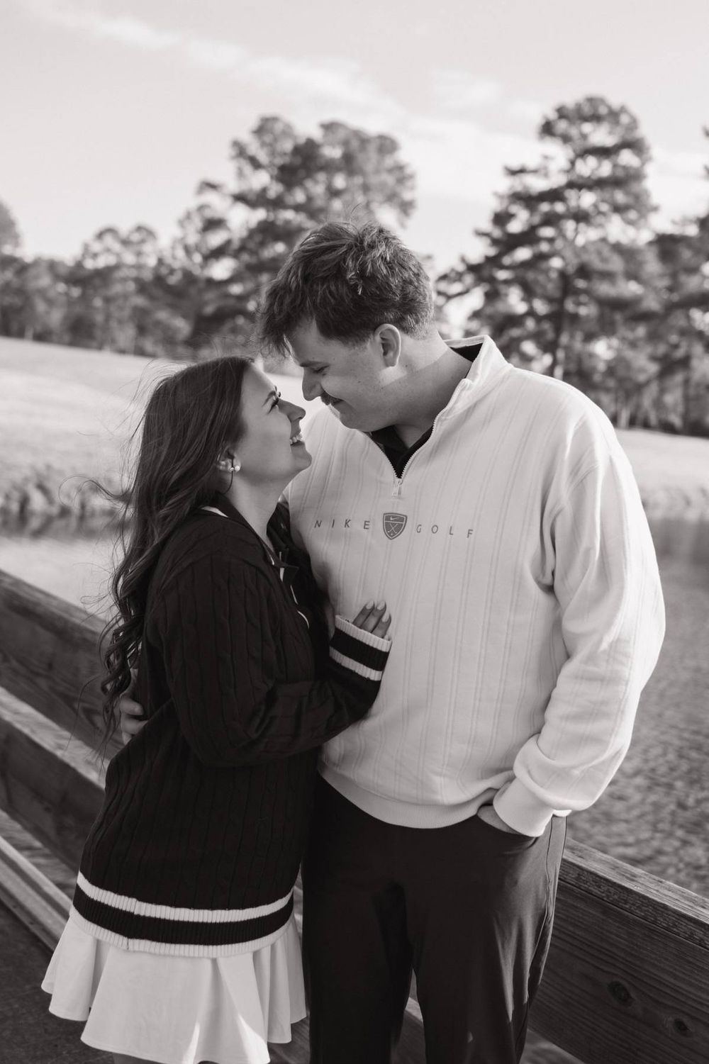 Black and white photo of a couple sharing a romantic moment by a wooden fence on a golf course, engagement session in North Carolina