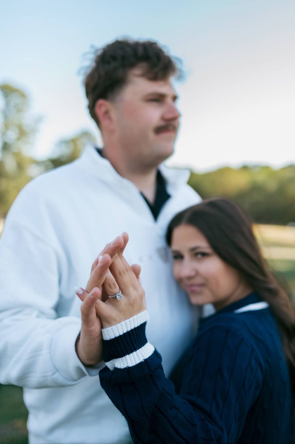 Engaged couple holding hands showing off diamond engagement ring at outdoor golf course photo session, engagement photographer NC