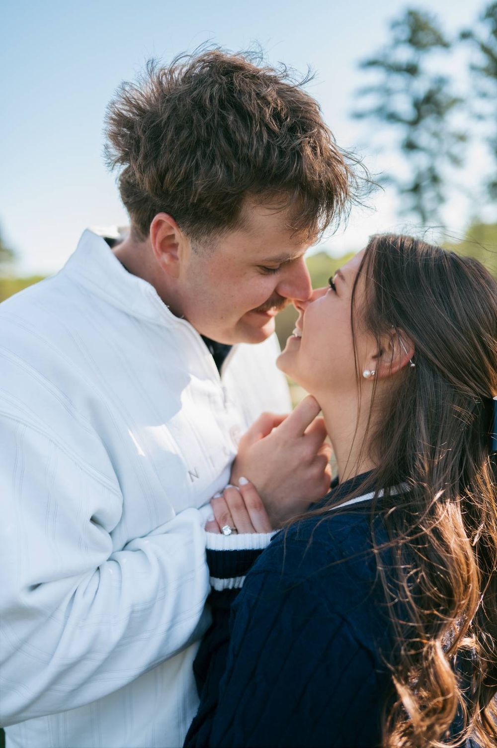 Close romantic couple nearly kissing outdoors in bright sunlight during engagement photo session in North Carolina