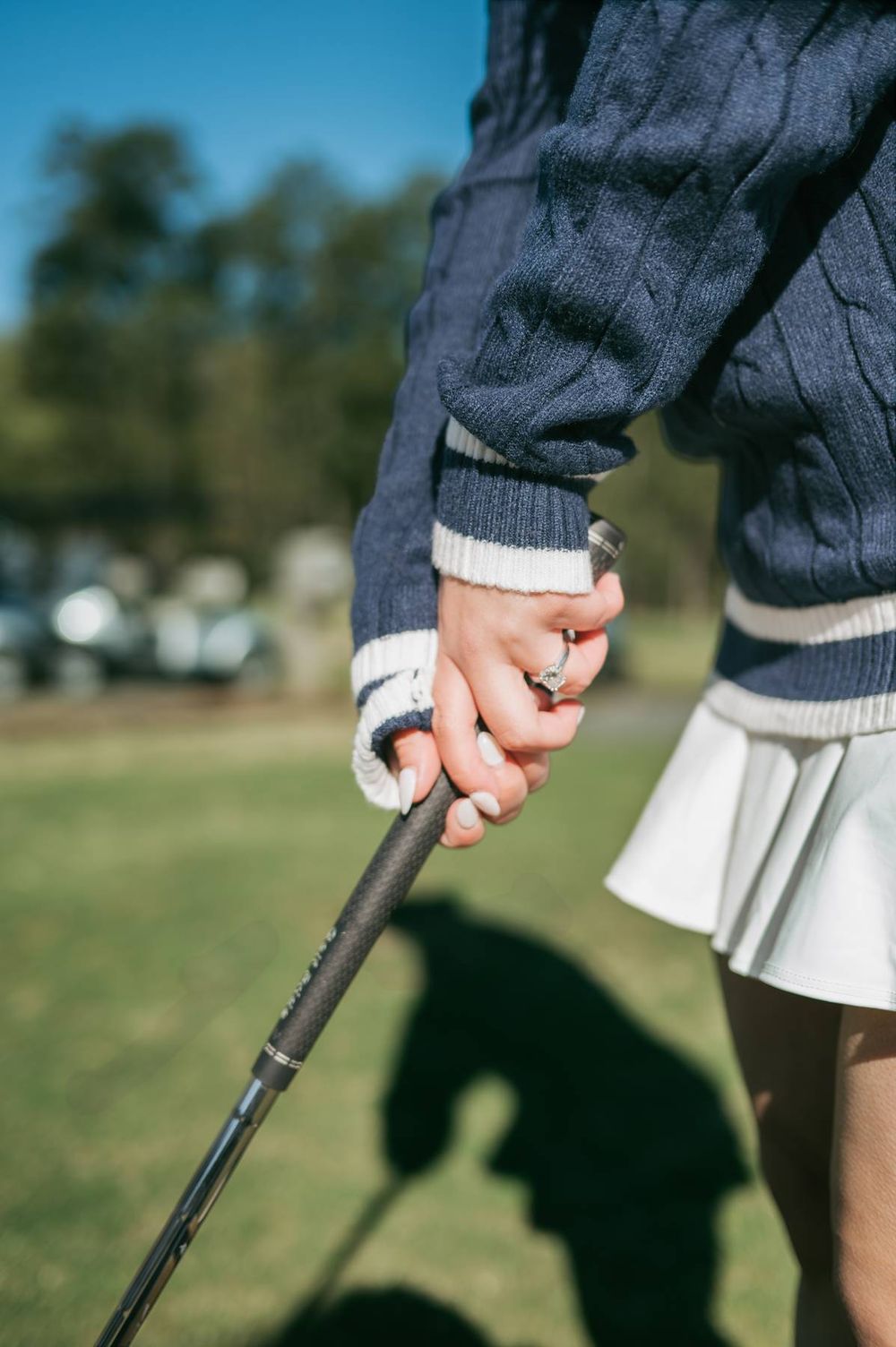 Close-up of woman holding a golf club wearing engagement ring and navy cable knit sweater, engagement photography Greensboro NC