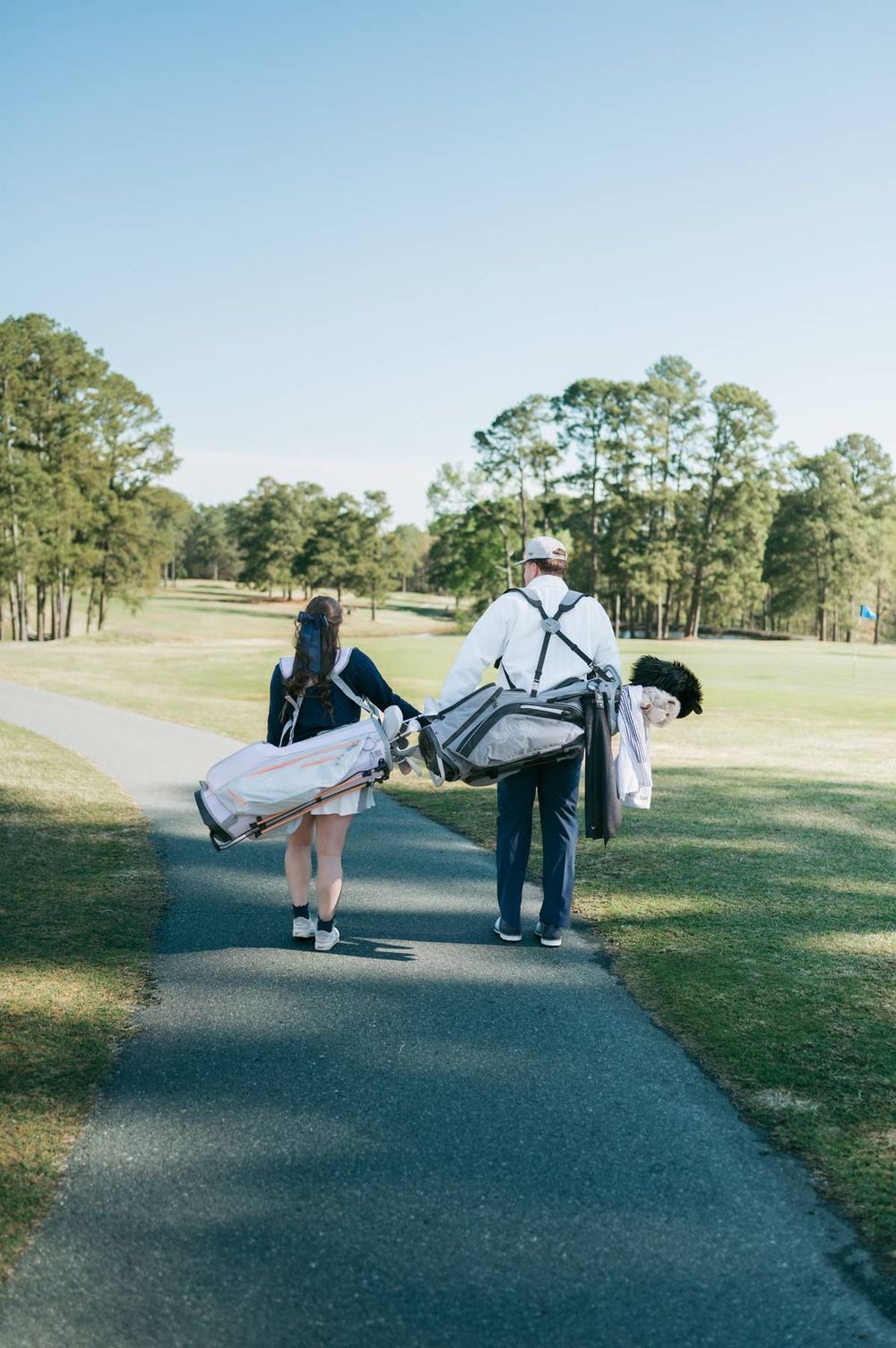 Couple walking down golf course path carrying golf bags during outdoor engagement photo session Asheboro NC