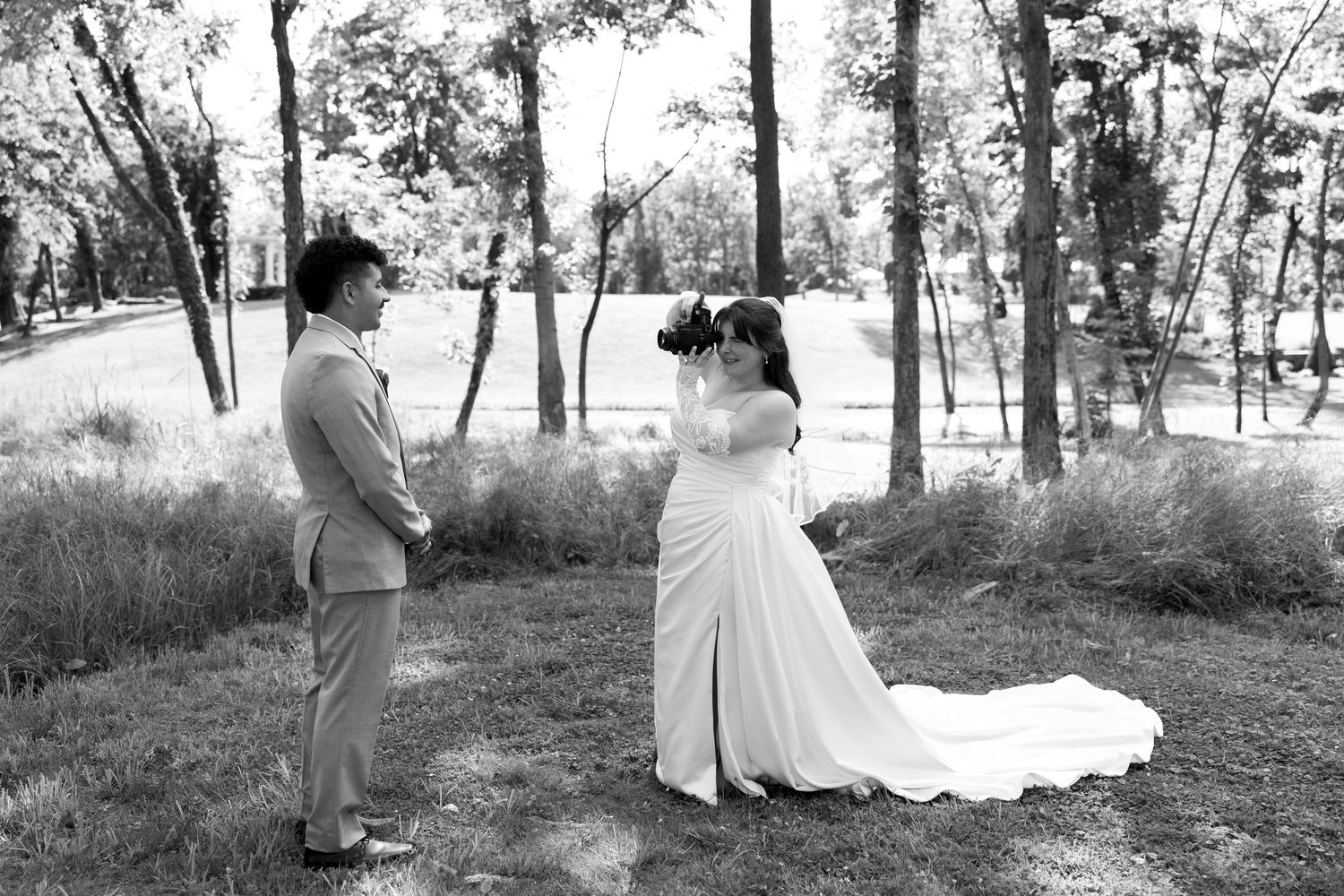 Black and white photo of a bride and groom sharing a first look moment outdoors among trees on their wedding day.
