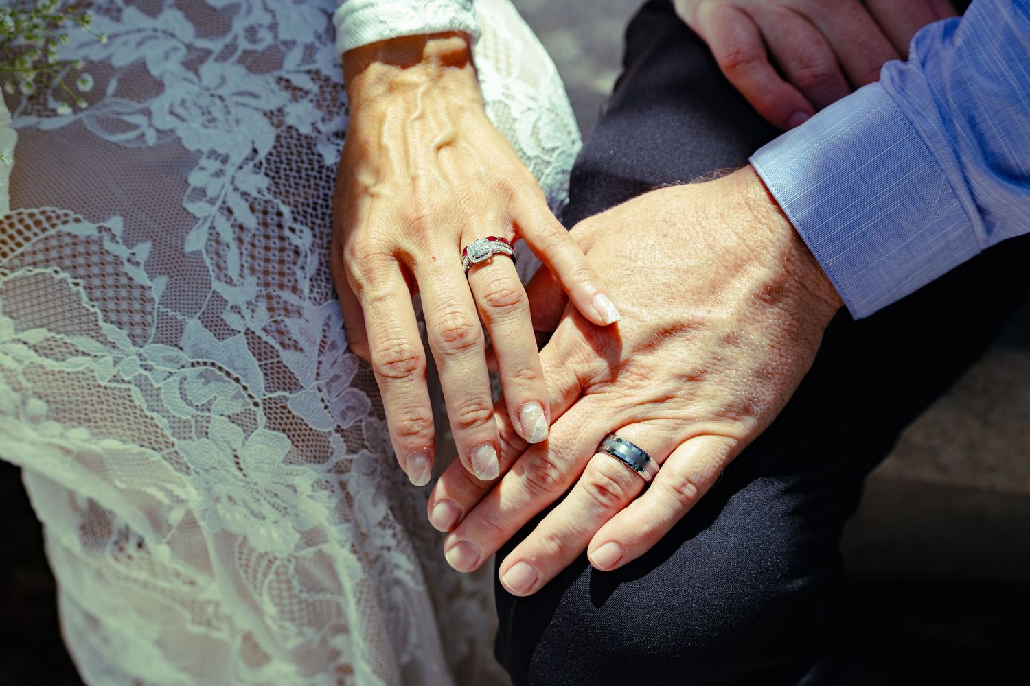 Newlywed couple displaying wedding rings with yellow rose bridal bouquet at outdoor ceremony.