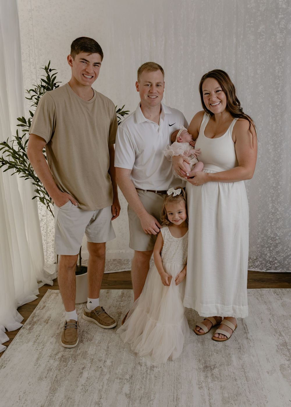 Family of four with newborn and young daughter posing in bright white studio.