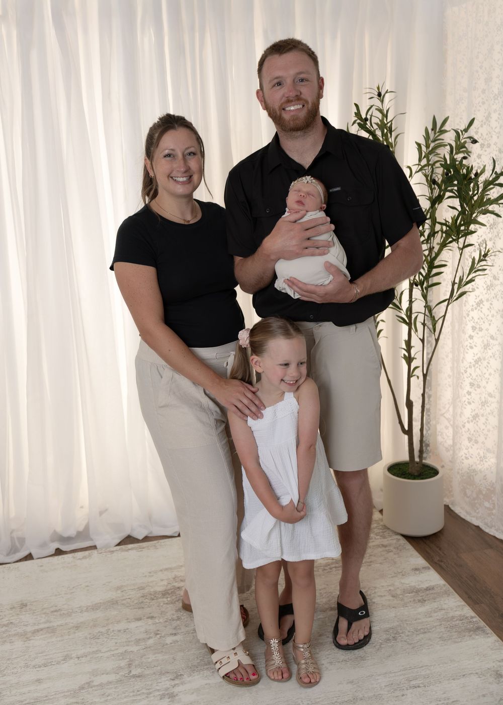 Family of four in matching black and white outfits with newborn in bright studio.