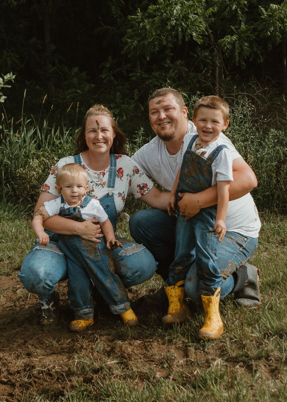 Family of four in denim overalls and yellow boots smiling outdoors in green setting.