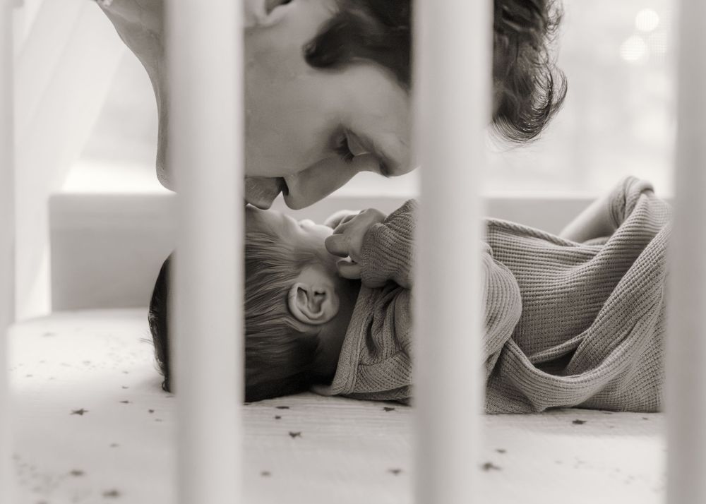 Black and white photo of a parent tenderly leaning over a newborn baby lying in a white crib.