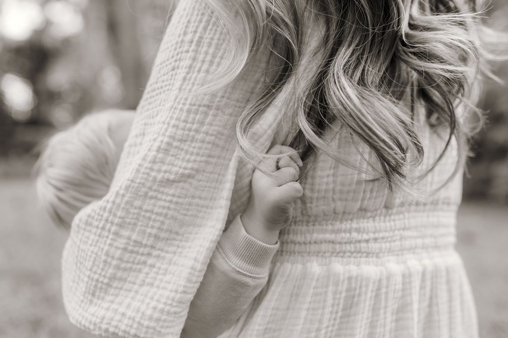 Black and white photo of a girl in a white smocked dress with wavy hair, standing outdoors.