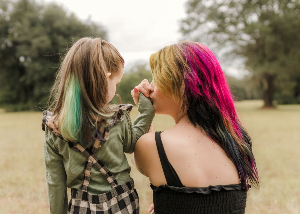 Mother and daughter with colorful dyed hair share a tender moment in a green field.