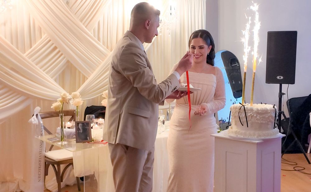 Bride and groom cutting wedding cake at elegant white-decorated reception venue with sparkling candles.