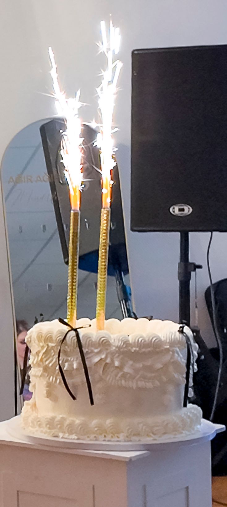 White celebration cake with sparkler candles shooting bright sparks, displayed on a pedestal at an elegant event venue.