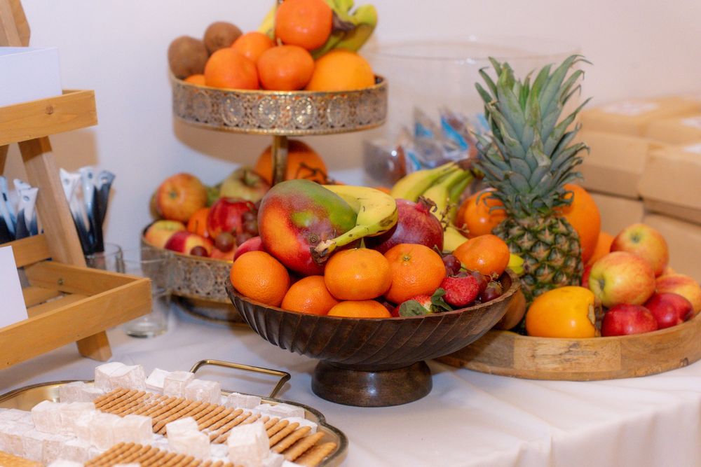 A colorful fruit display with oranges, apples, bananas, and a pineapple arranged in decorative bowls on a white table.