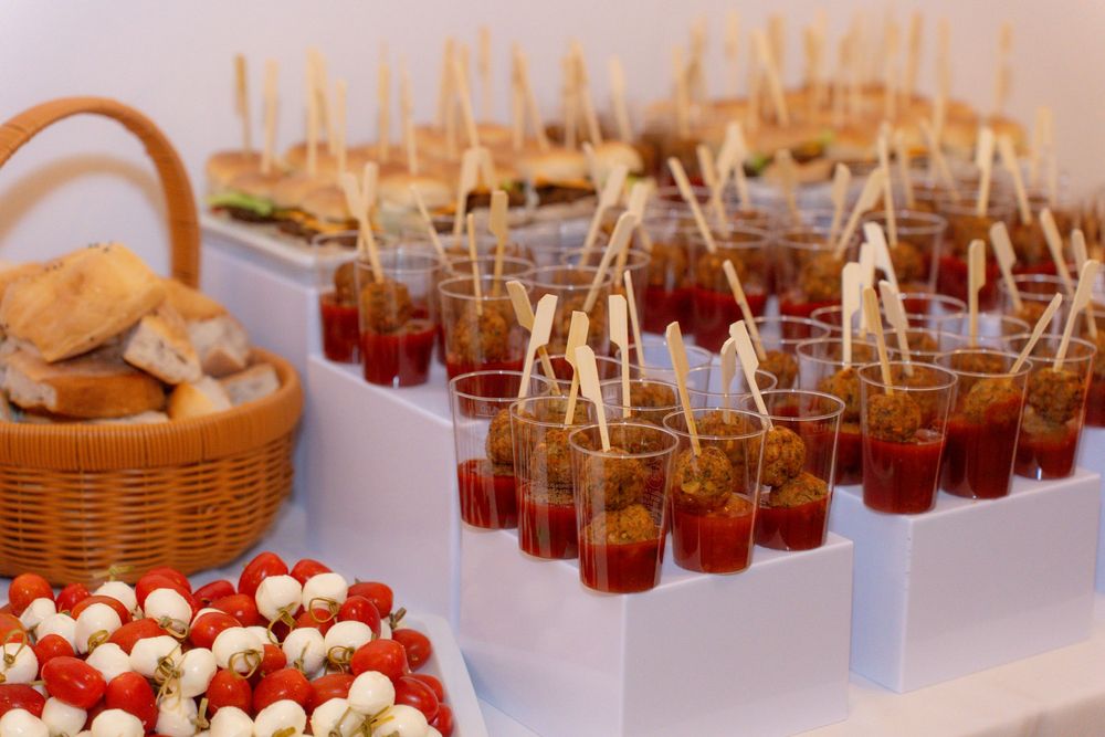 Elegant catering display with tomato appetizers in cups, skewers, caprese salad, and bread basket at an event.