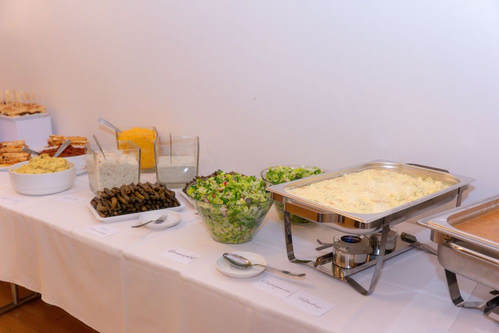 Buffet table with chafing dishes, green salad, olives, and assorted food items on a white tablecloth.