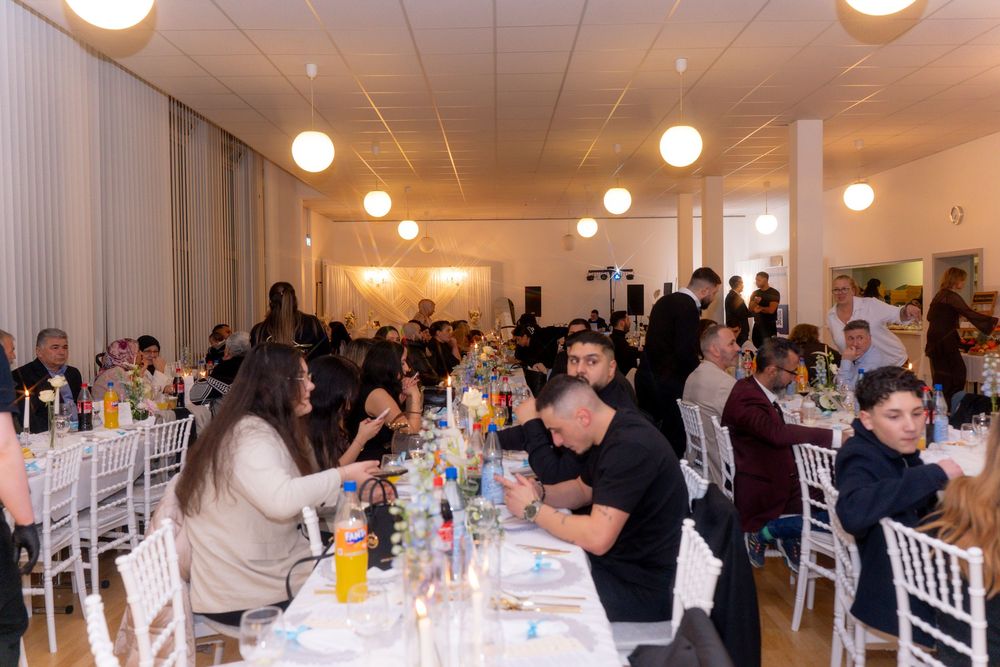 Guests dining at a formal banquet event in a bright hall with white chairs and round tables.