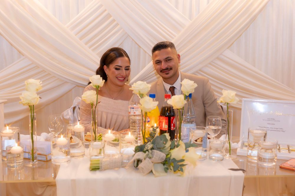 Bride and groom smiling together at elegant wedding reception table with white roses and candles.