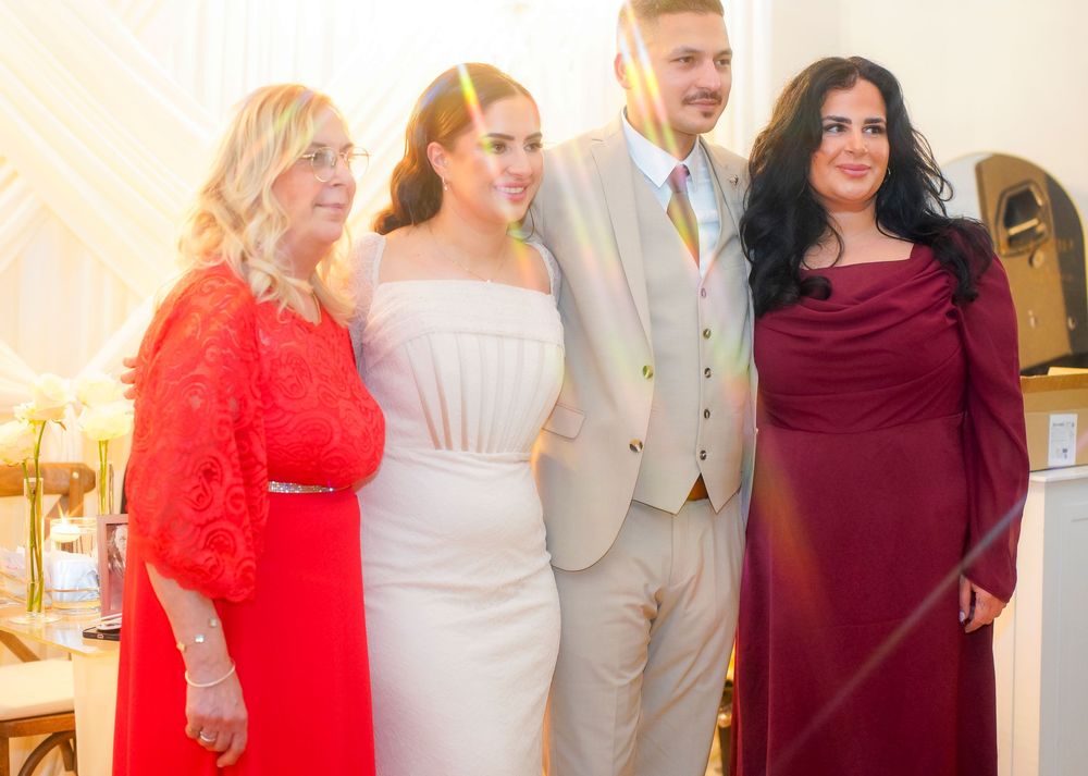 Four people posing together at a wedding, with the bride in white and guests in red and burgundy formal attire.