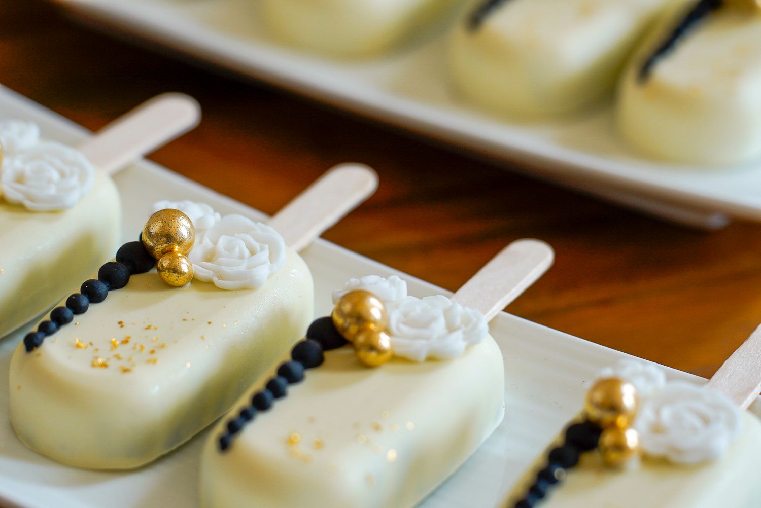 Luxury white chocolate wedding cake pops decorated with gold pearls and white sugar roses on a white plate.