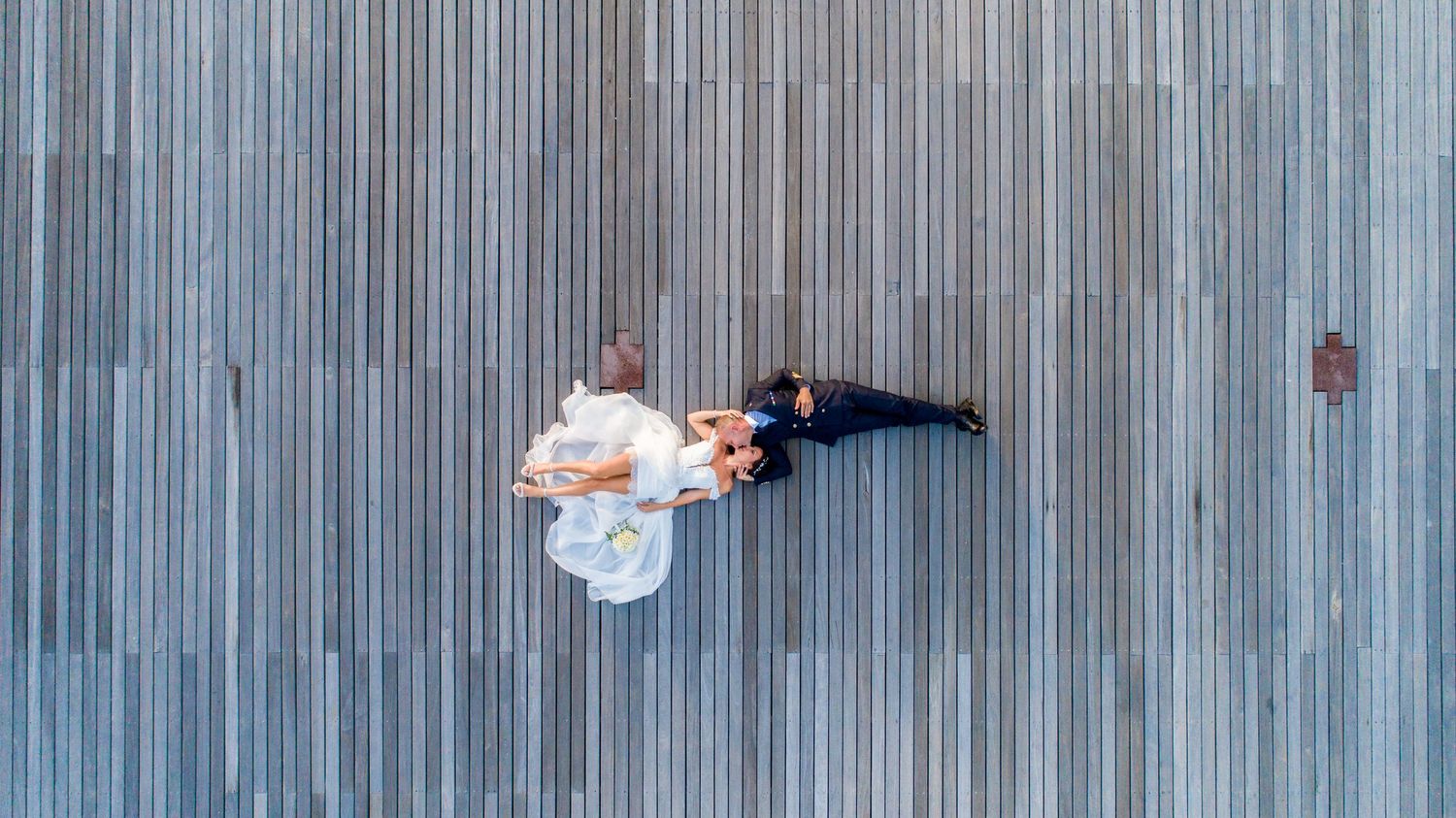 Drone shot of bride and groom lying on wooden decking during a destination wedding portrait session in Mauritius, Luminair Studio