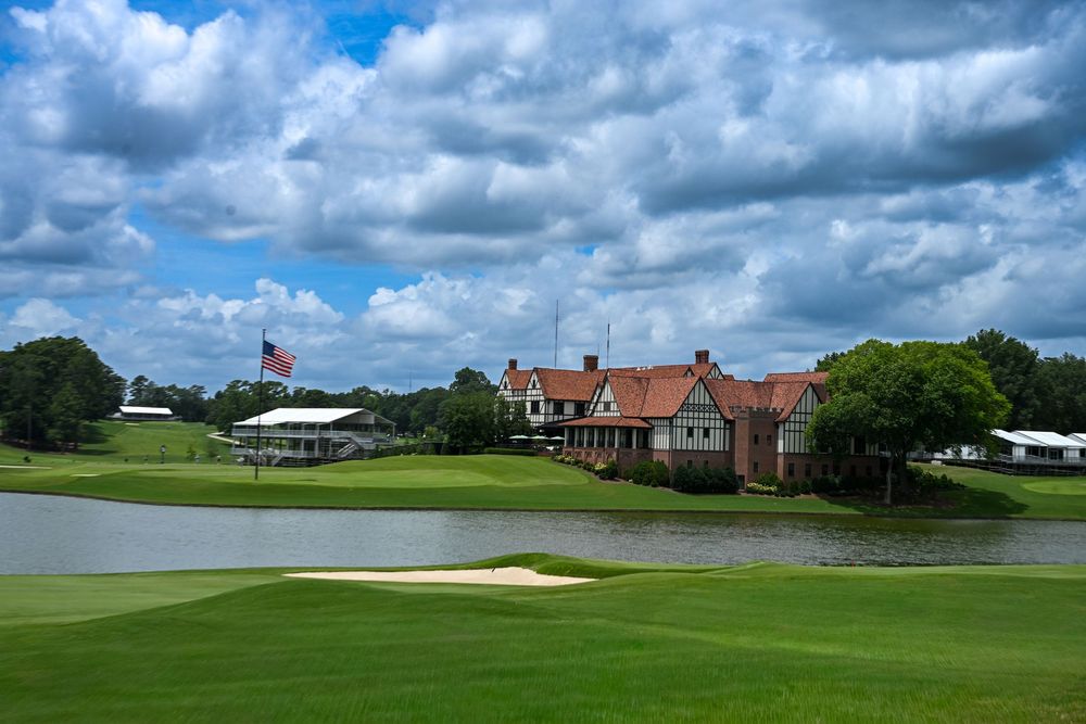 Scenic golf course with sand bunker, water hazard, and clubhouse under dramatic cloudy sky.