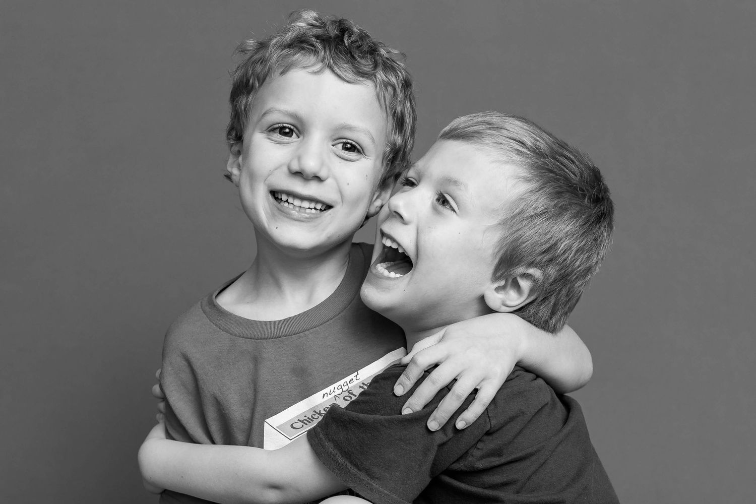Two happy young boys hugging and laughing together in a black and white portrait photo.