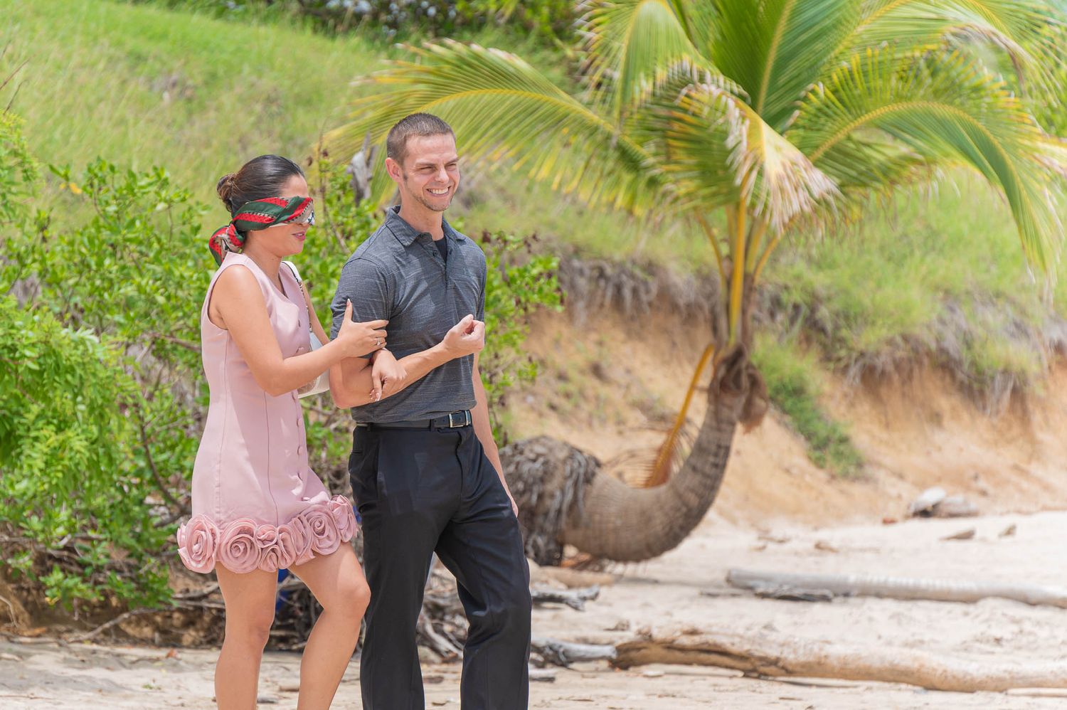 Couple dancing together on a tropical beach with palm trees and lush greenery in the background.