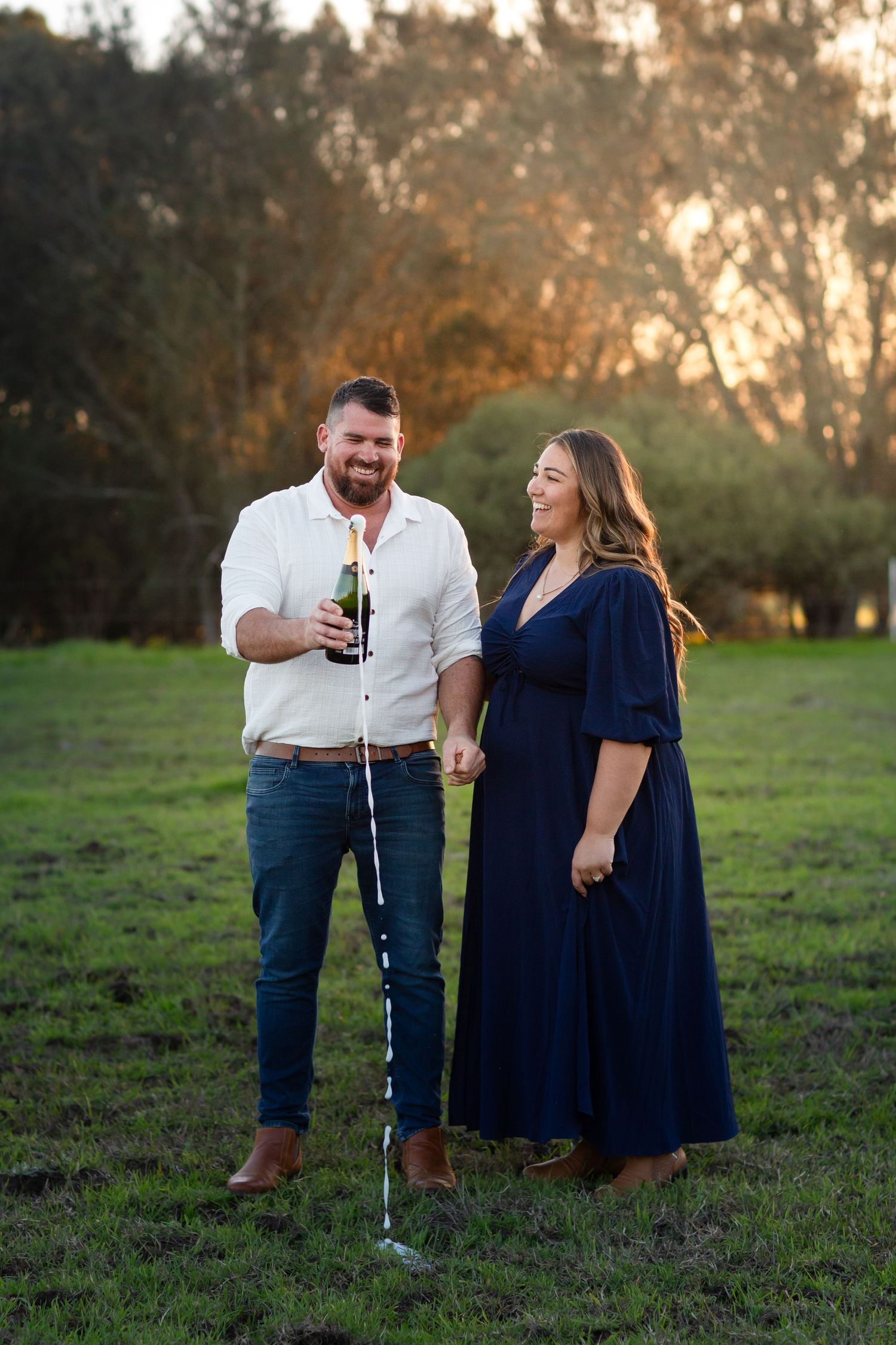 Couple popping a bottle of champagne in a paddock during golden hour in Perth