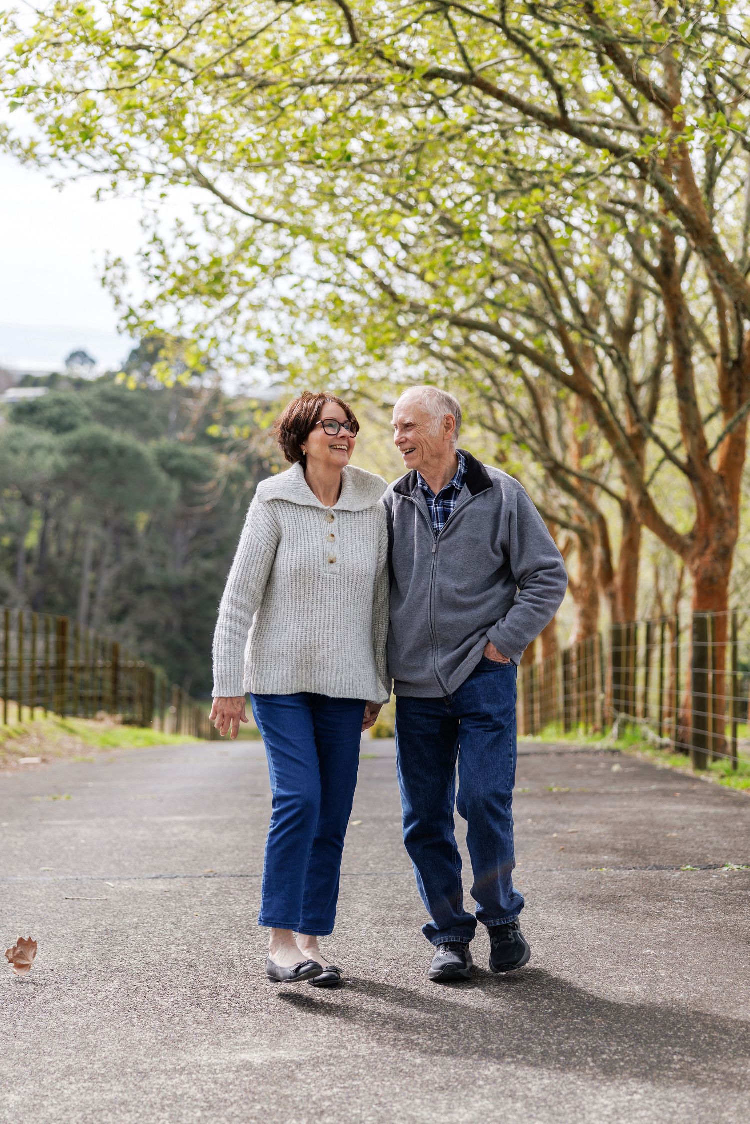 Couple holding hands and walking under tall trees in Auckland