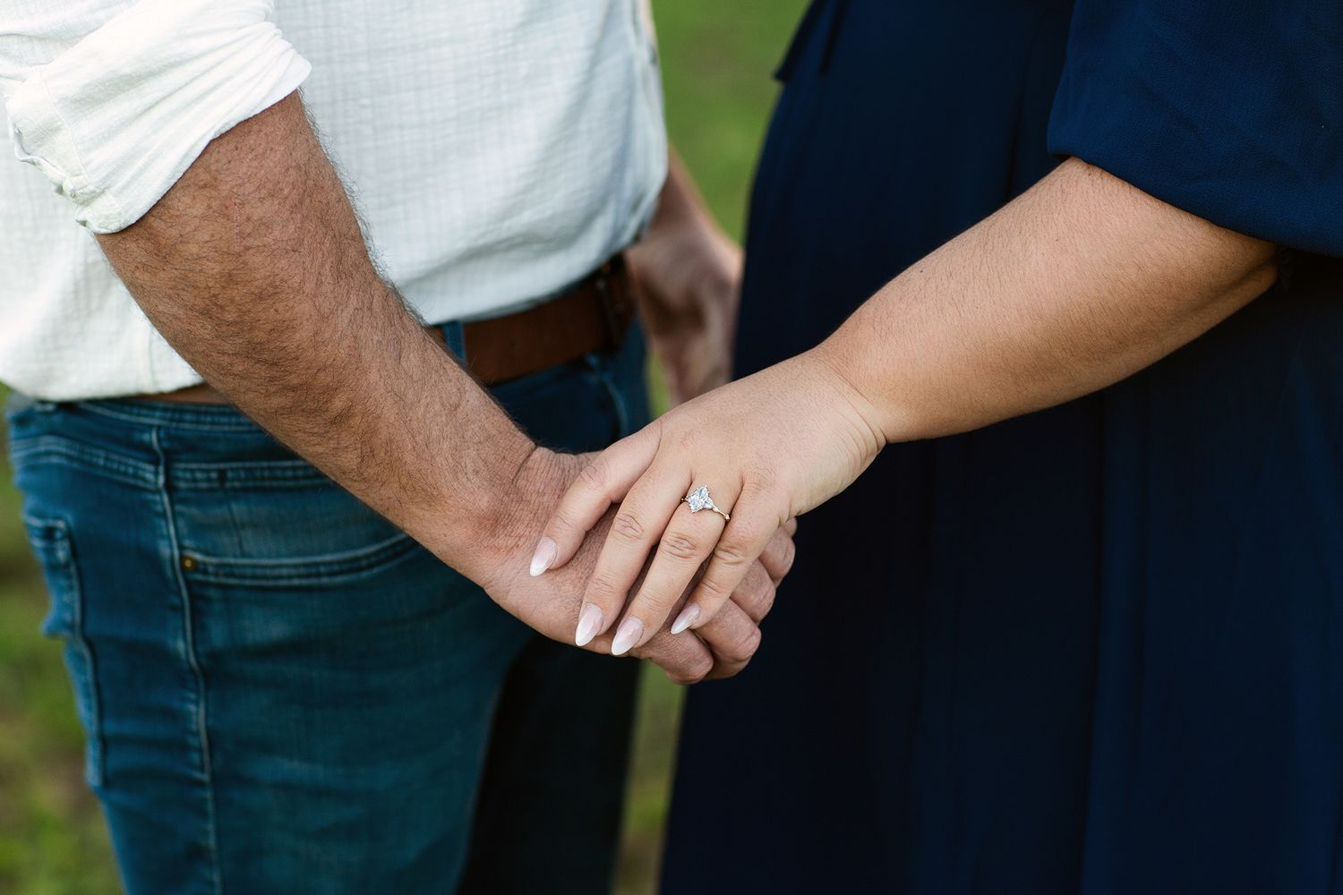 Engagement ring on display while couples hold hands during engagement session in paddock in Perth