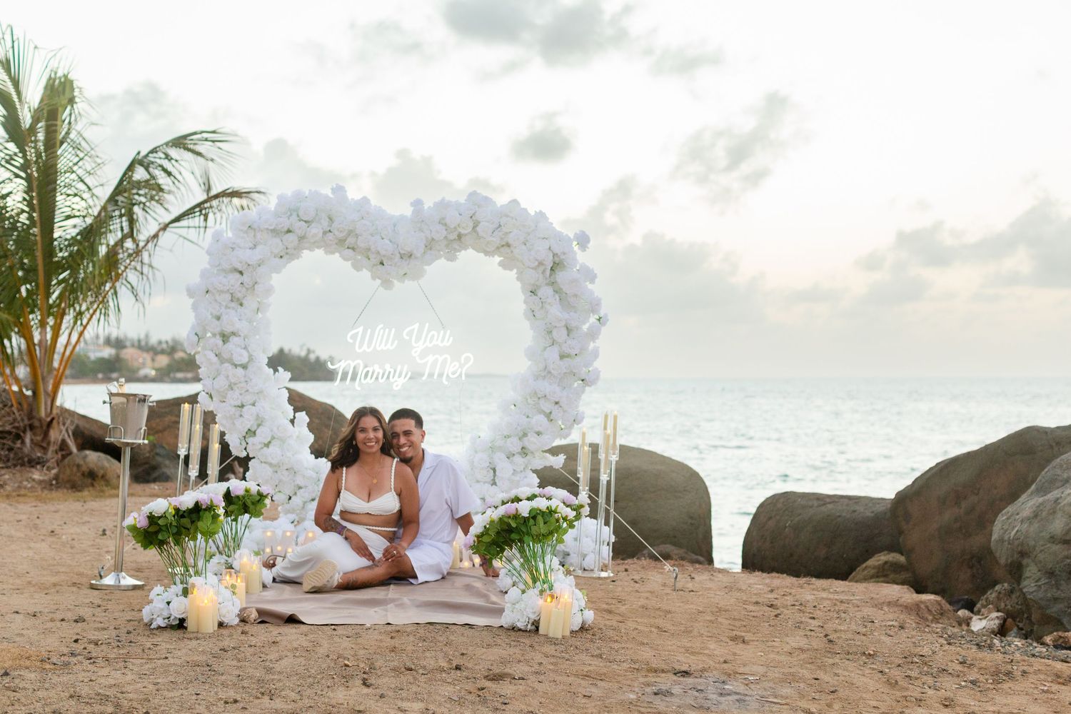 Marriage proposal. Man, woman, and decorative setup with white flower heart overlooking the ocean in Río Grande, Puerto Rico.