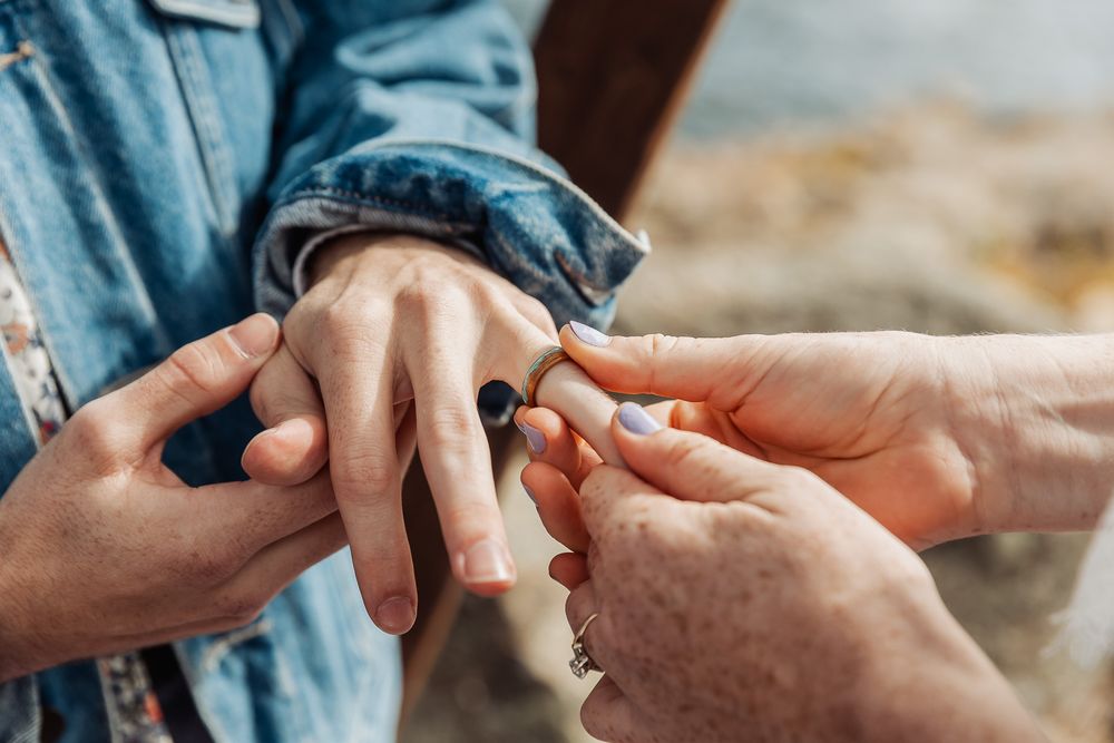 Close-up of a person placing a ring on another person's finger during a romantic marriage proposal outdoors.