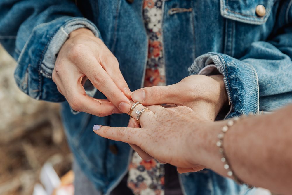 Close-up of a couple exchanging a silver wedding ring during a romantic outdoor proposal.