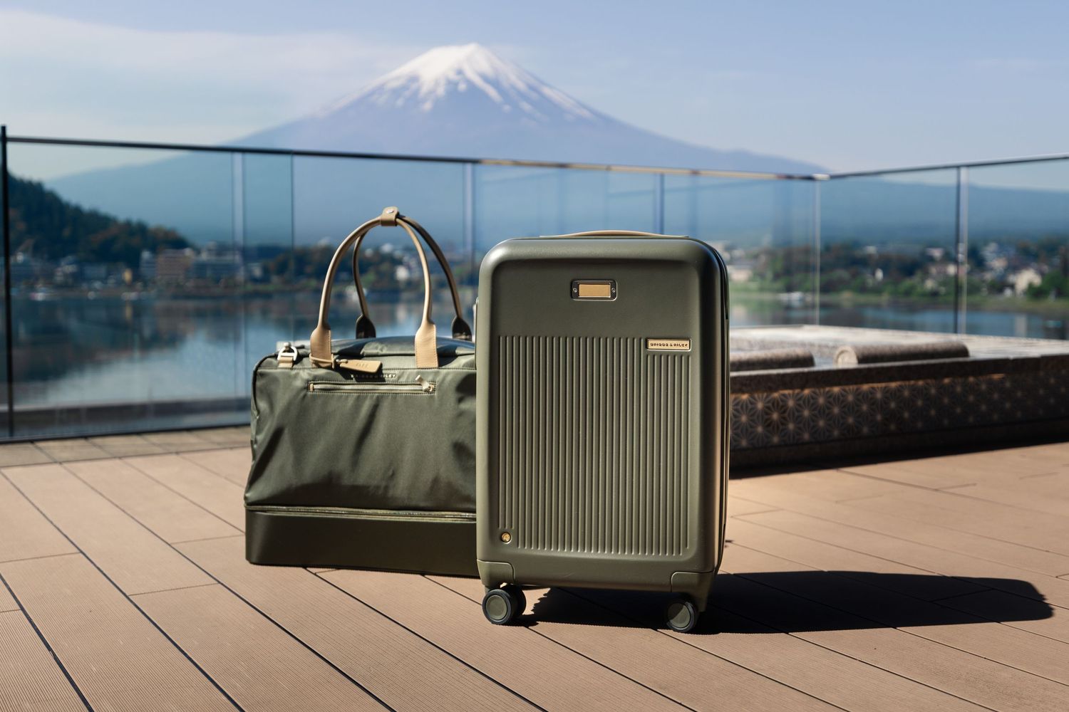 Olive green luggage set with carry-on and duffel bag on a deck overlooking Mount Fuji, Japan.