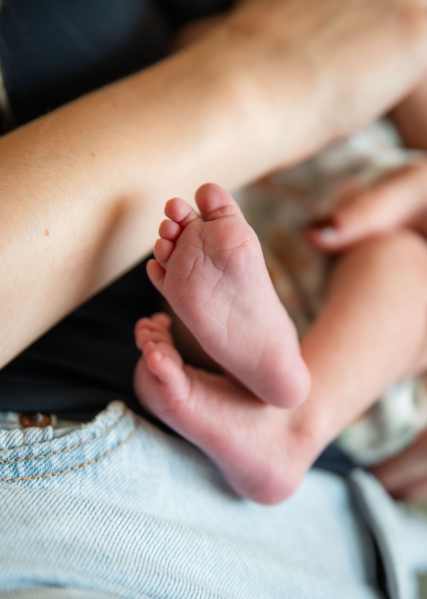Close-up of tiny newborn baby feet resting on a parent's lap in soft natural light.