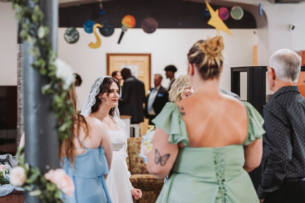 Bride in white gown and veil chatting with bridesmaids in blue and green dresses at a decorated wedding reception.