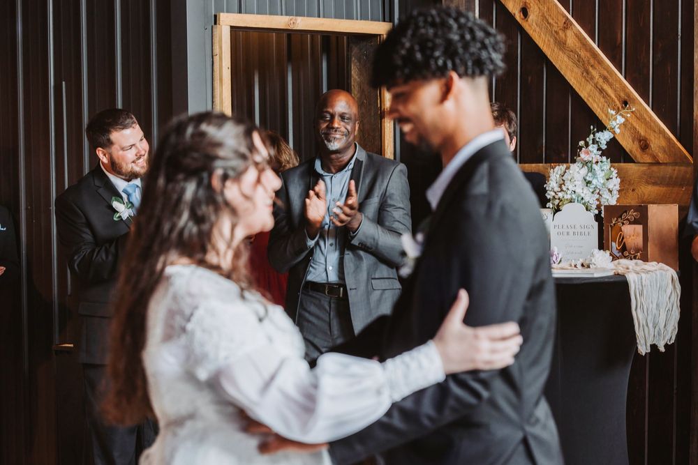 Couple shares first dance at rustic barn wedding while guests clap and celebrate in the background.