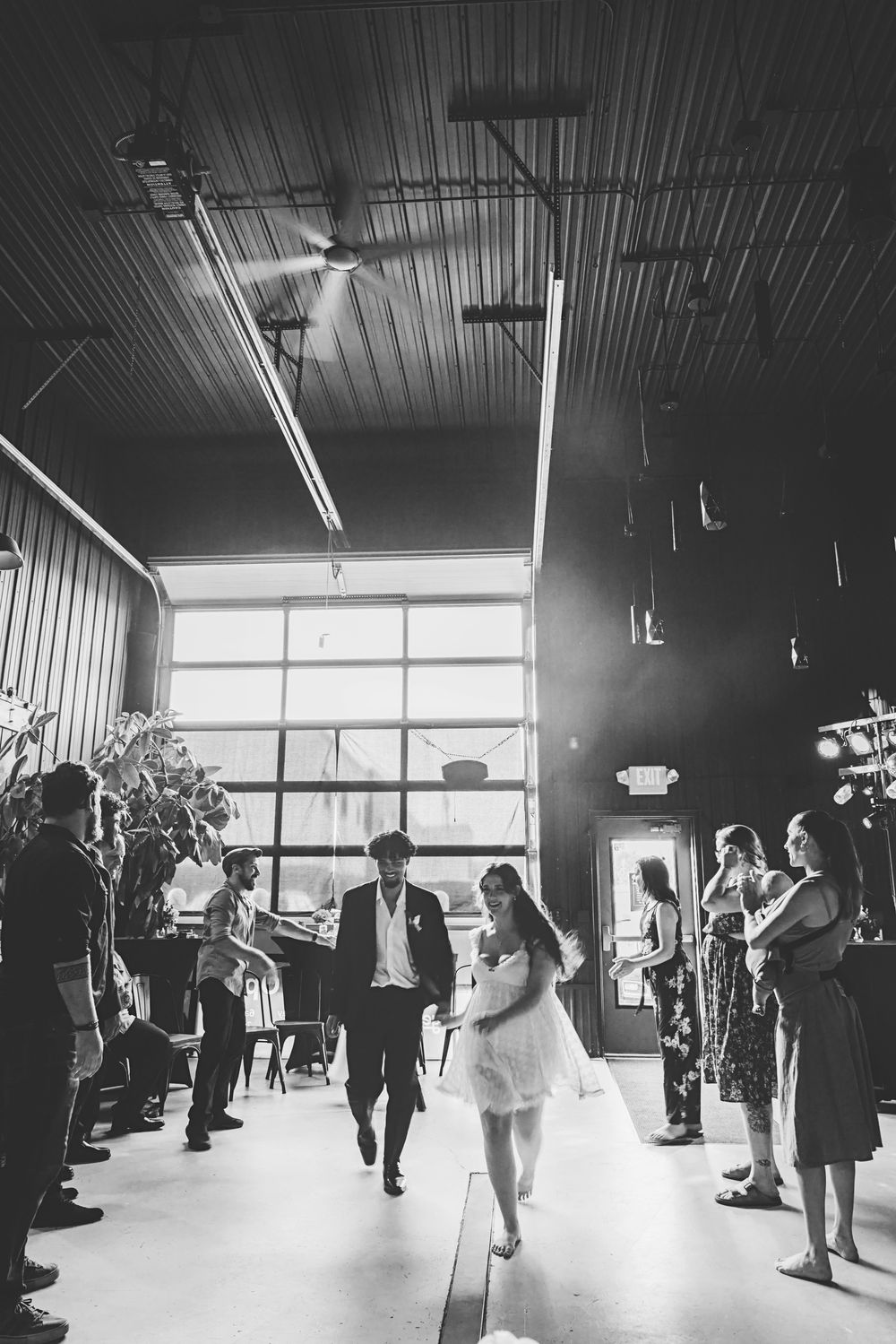 Black and white photo of a bride and groom walking down the aisle in an industrial wedding venue.