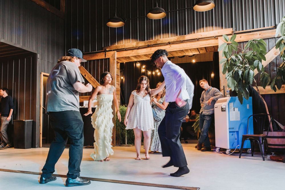 Guests dancing joyfully inside a rustic barn venue during a lively wedding reception celebration.