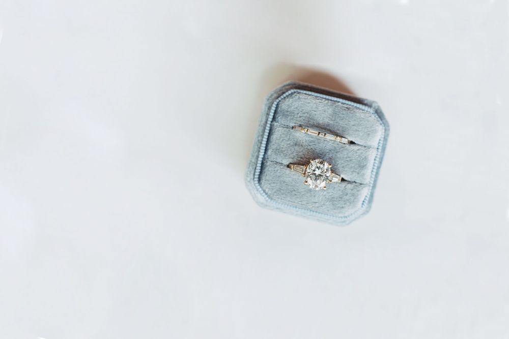 Diamond engagement ring and wedding band displayed in a blue velvet ring box on a white background.