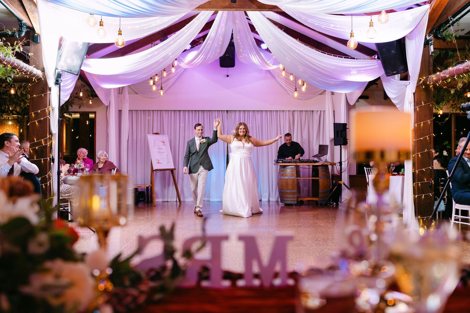 Bride and groom share first dance under draped white fabric canopy with string lights at elegant wedding reception.