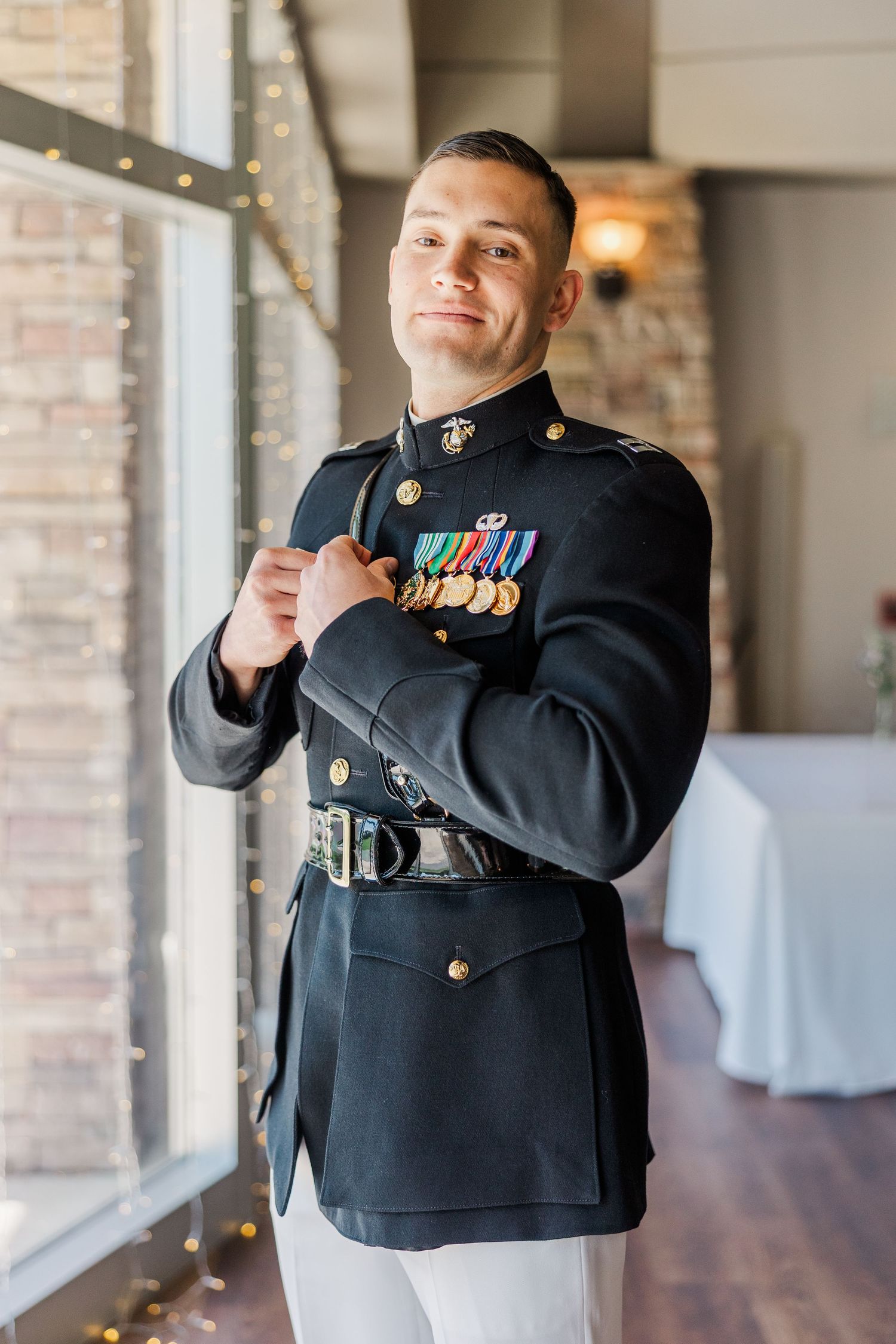 Marine in dress blues uniform with medals smiling confidently indoors near large windows.