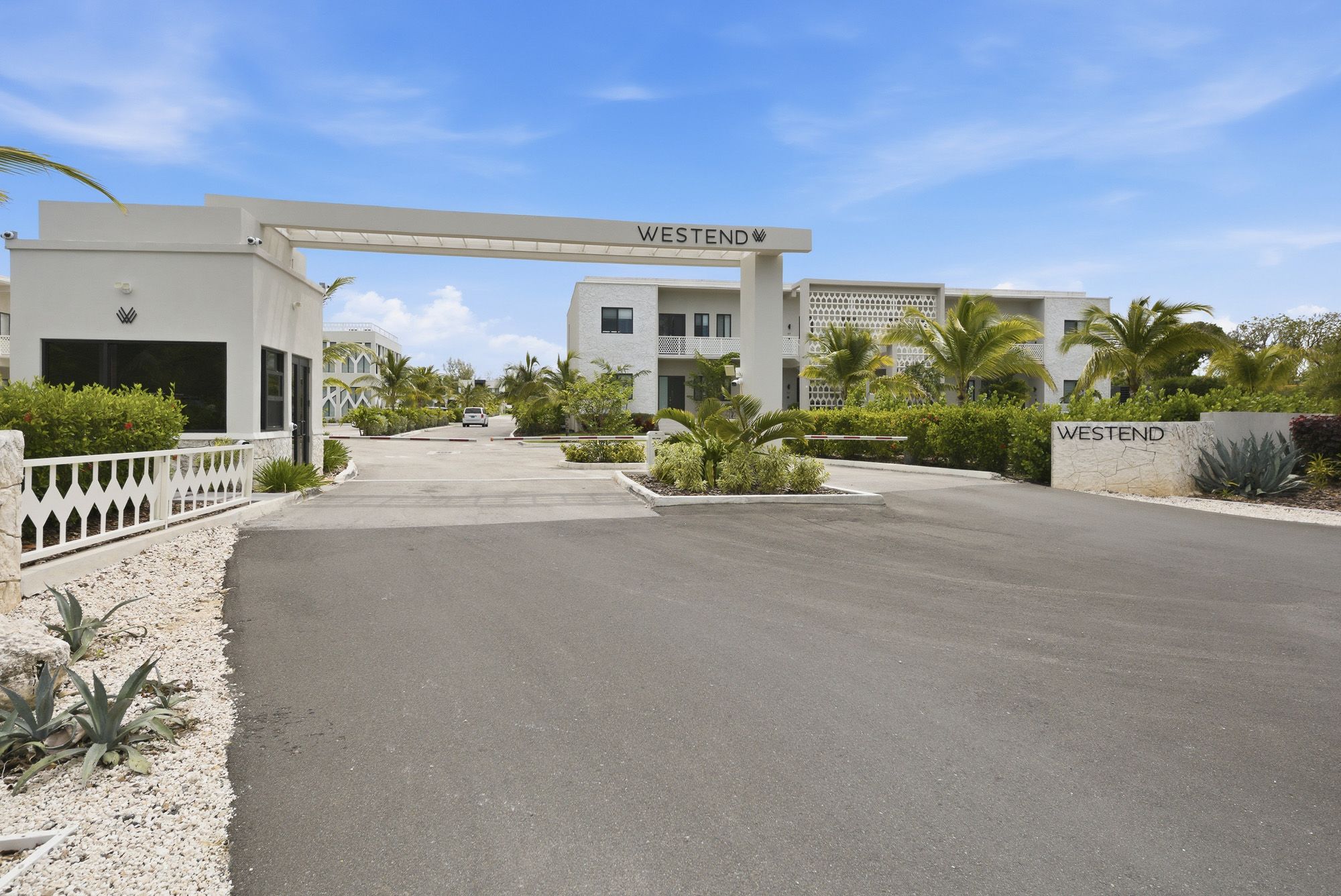 Westend gated community entrance with white archway, palm trees, and manicured landscaping under a bright blue sky.
