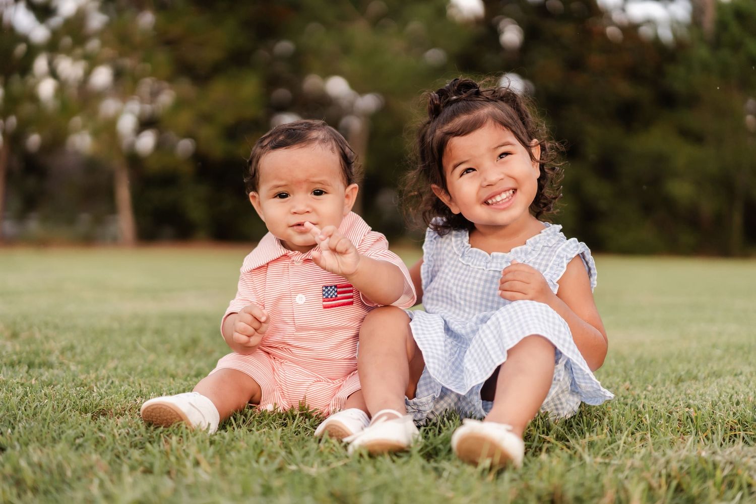 Three people in blue outfits sit together outdoors on a bench during golden hour lighting in a park setting.