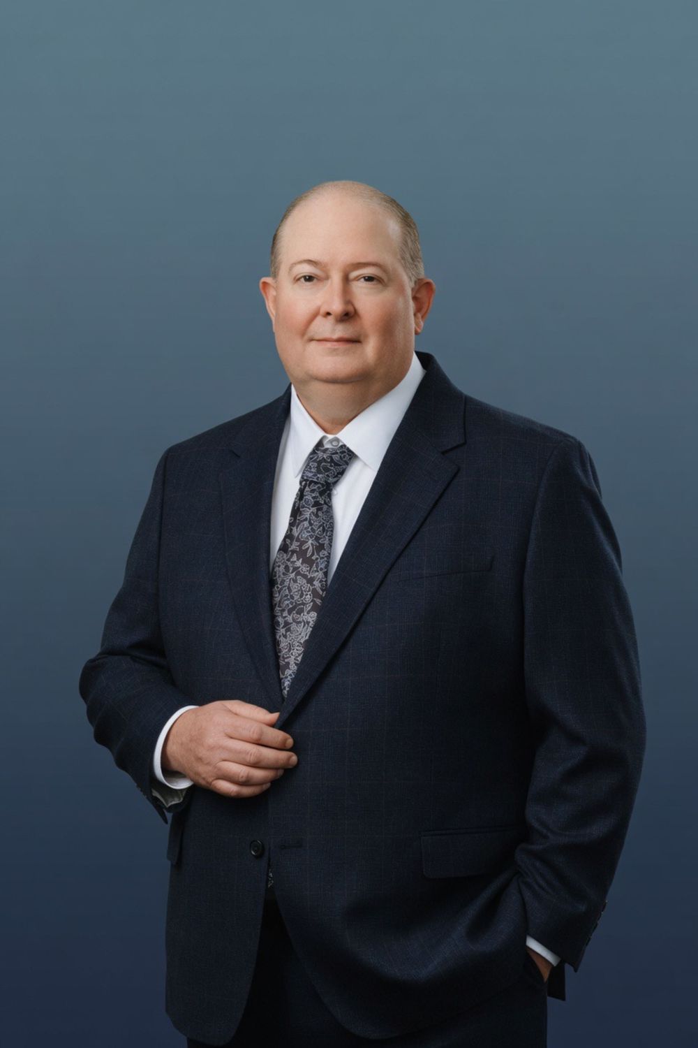 Professional man in navy suit and patterned tie poses confidently for a formal business portrait.
