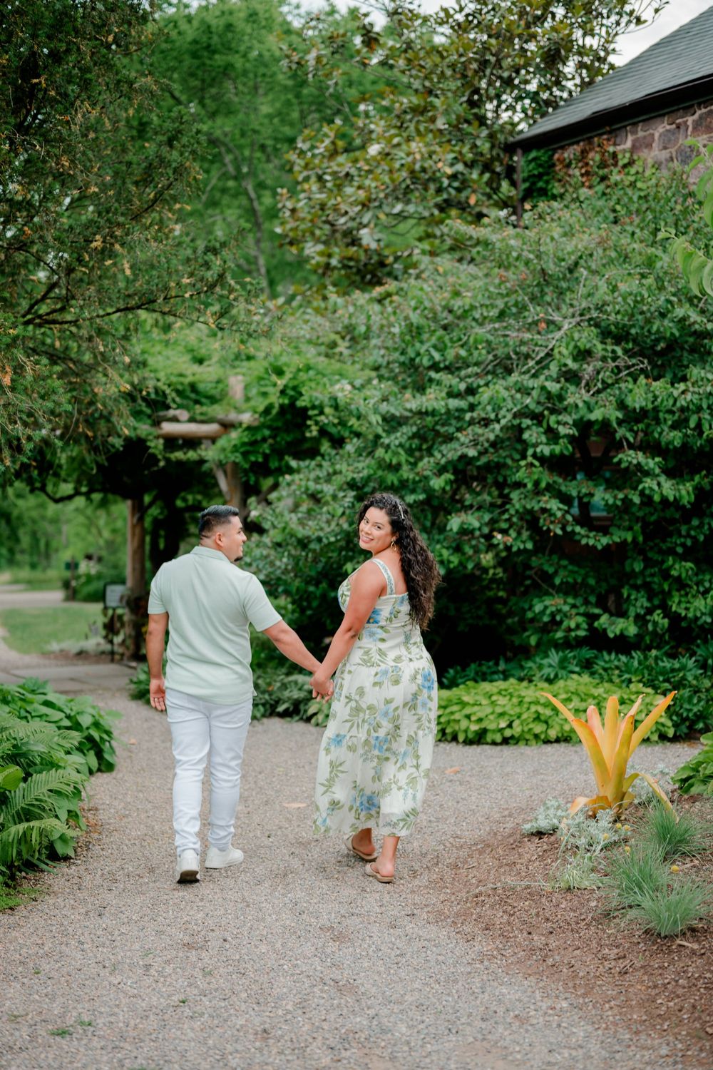 Engaged couple holding hands while strolling down a garden gravel path at Willowwood Arboretum in Far Hills, New Jersey.