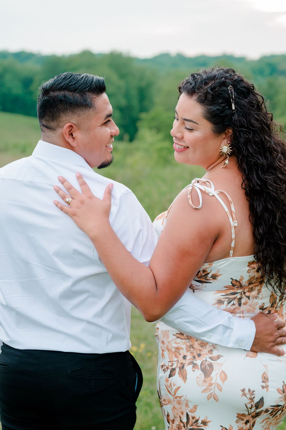 Bride-to-be resting her hand on her fiancé’s shoulder while looking back lovingly in an open meadow at Willowwood Arboretum, NJ.