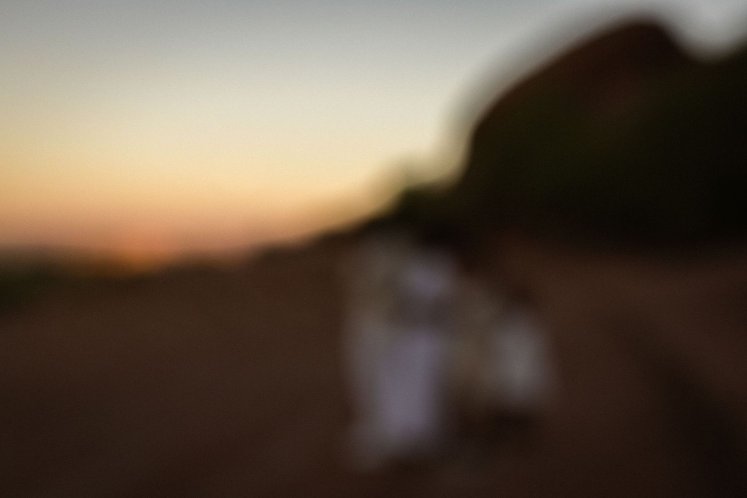 Blurry silhouette of a person in white dress at golden sunset in an open field.