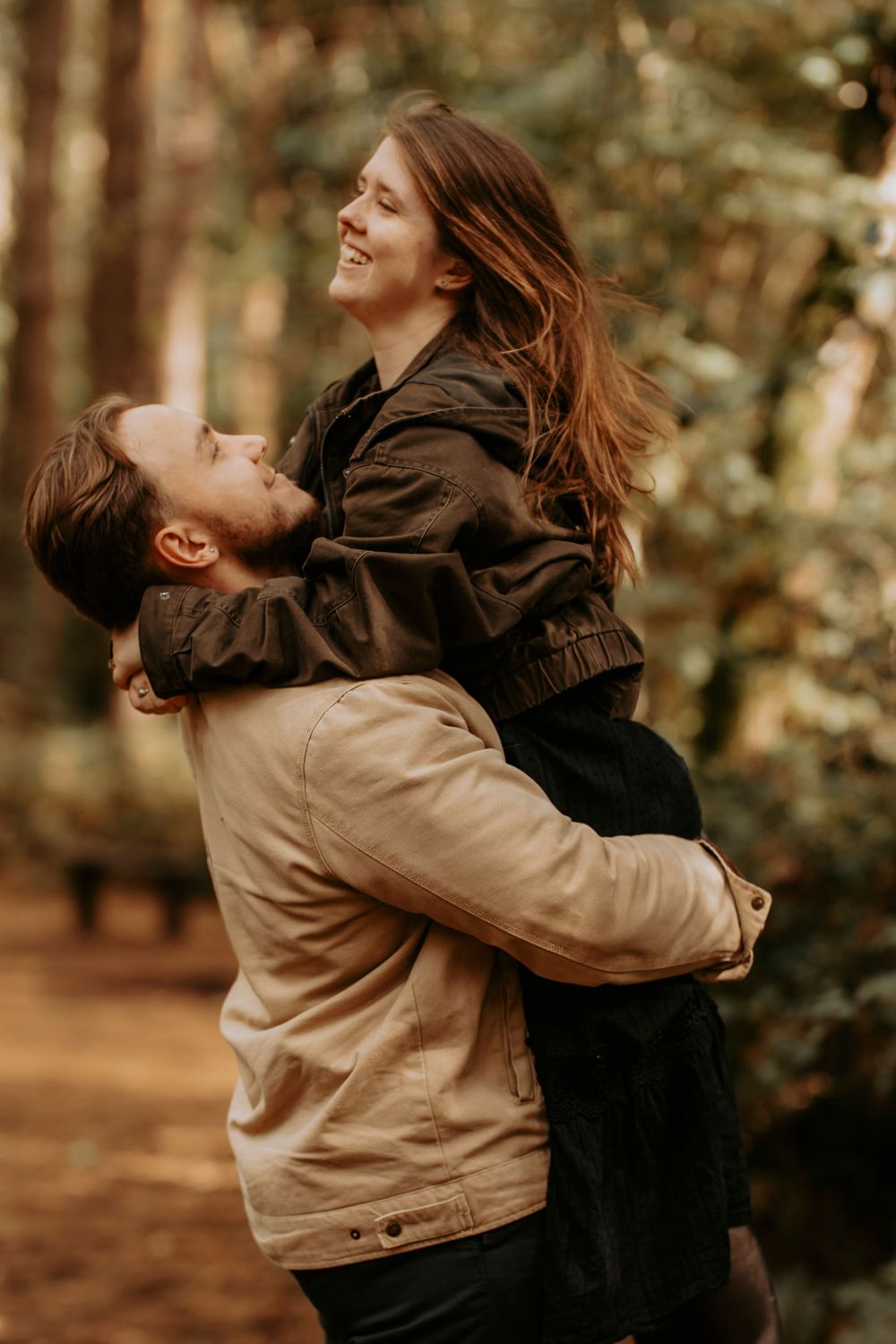 Man lifting smiling woman in his arms in a romantic forest setting with warm autumn tones.