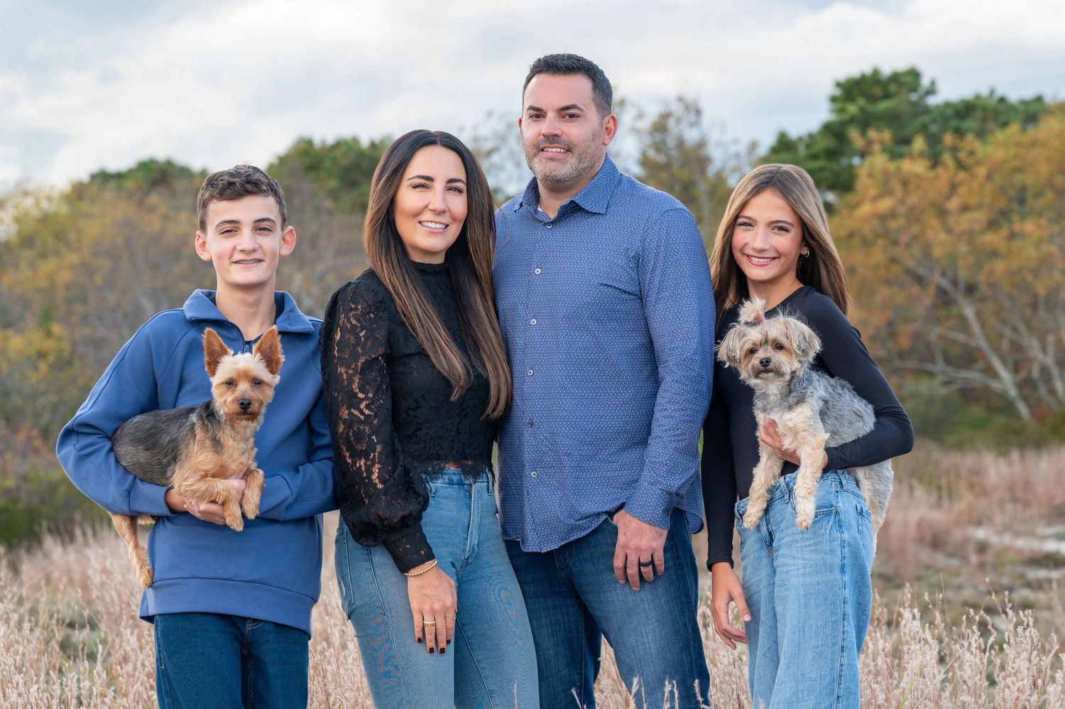 Happy family of five posing together on a wooden bridge surrounded by autumn trees.