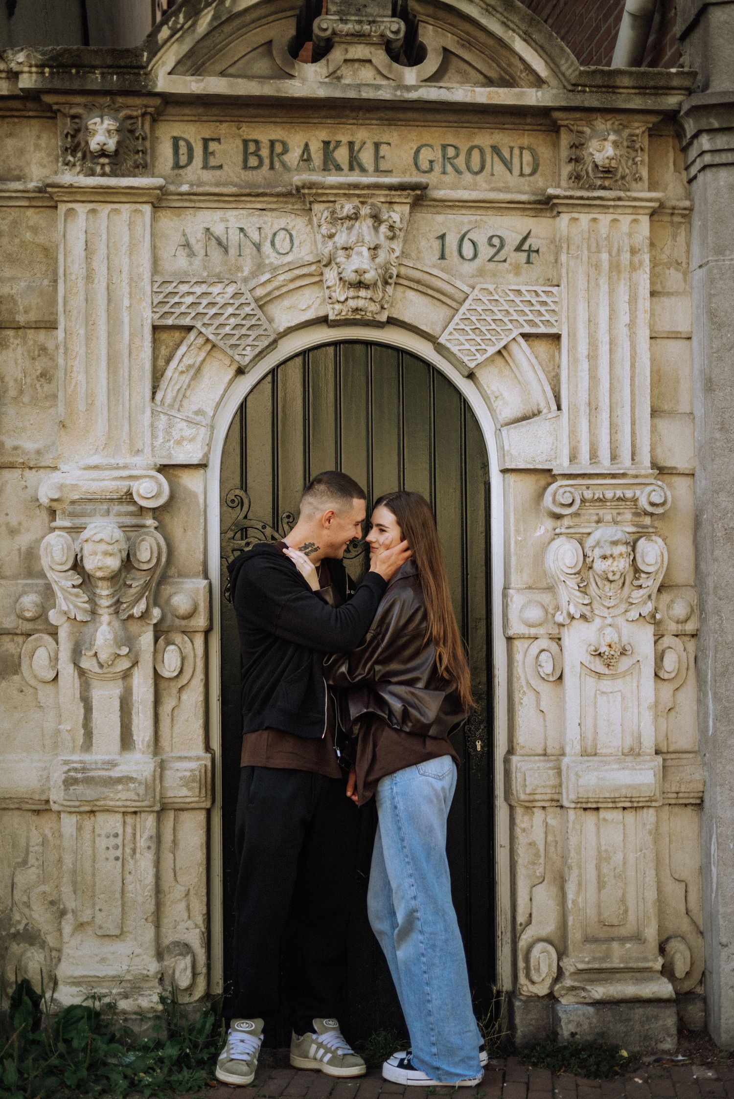 Couple embracing and kissing in front of the historic De Brakke Grond doorway, an ornate stone archway dated Anno 1624. Amsterdam, Rokin